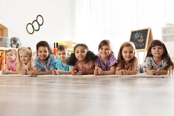 Groep schattige kleine kinderen liggend op de vloer binnenshuis. Kleuterschool speeltijd activiteiten — Stockfoto