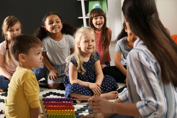 Nette kleine Kinder mit Kindergärtnerin im Kindergarten. Aktivitäten in Innenräumen — Stockfoto