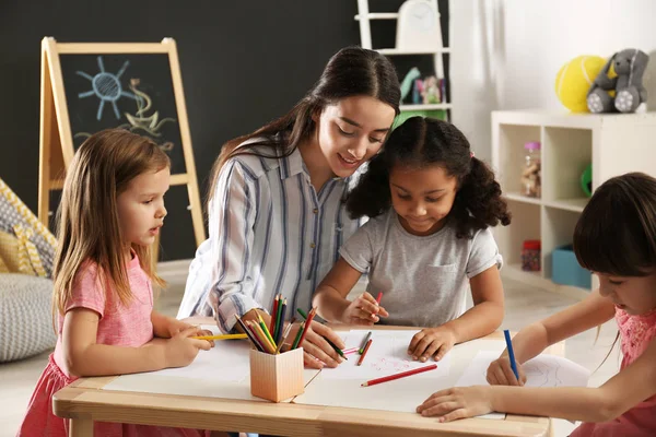 Niedliche kleine Kinder mit Kindergärtnerin malen am Tisch im Kindergarten. Aktivitäten in Innenräumen — Stockfoto