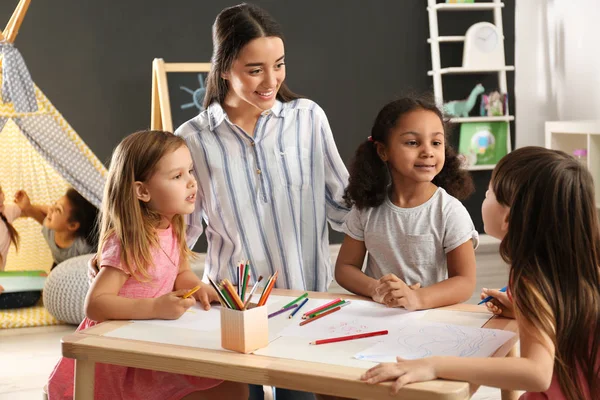 Lindos niños pequeños con maestra de guardería dibujando en la mesa en el jardín de infantes. Actividad interior —  Fotos de Stock