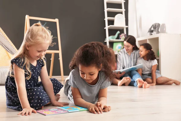 Niedliche kleine Kinder lesen Buch auf dem Fußboden im Kindergarten, Platz für Text. Aktivitäten in Innenräumen — Stockfoto