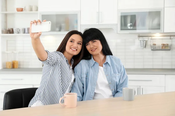 Jovem mulher e sua mãe madura tomando selfie na mesa dentro de casa — Fotografia de Stock