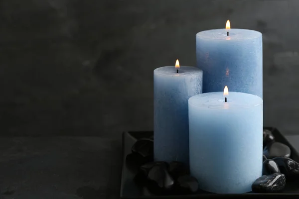 Tmavá deska se třemi hořícími svíčkami a kameny na stole, prostor pro text — Stock fotografie