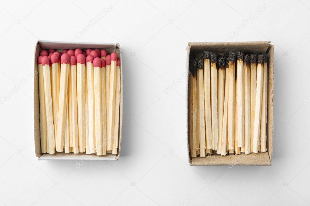 Cardboard boxes with whole and burnt matches on white background, top view