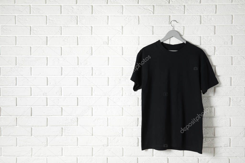 Hanger with black t-shirt against brick wall. Mockup for design