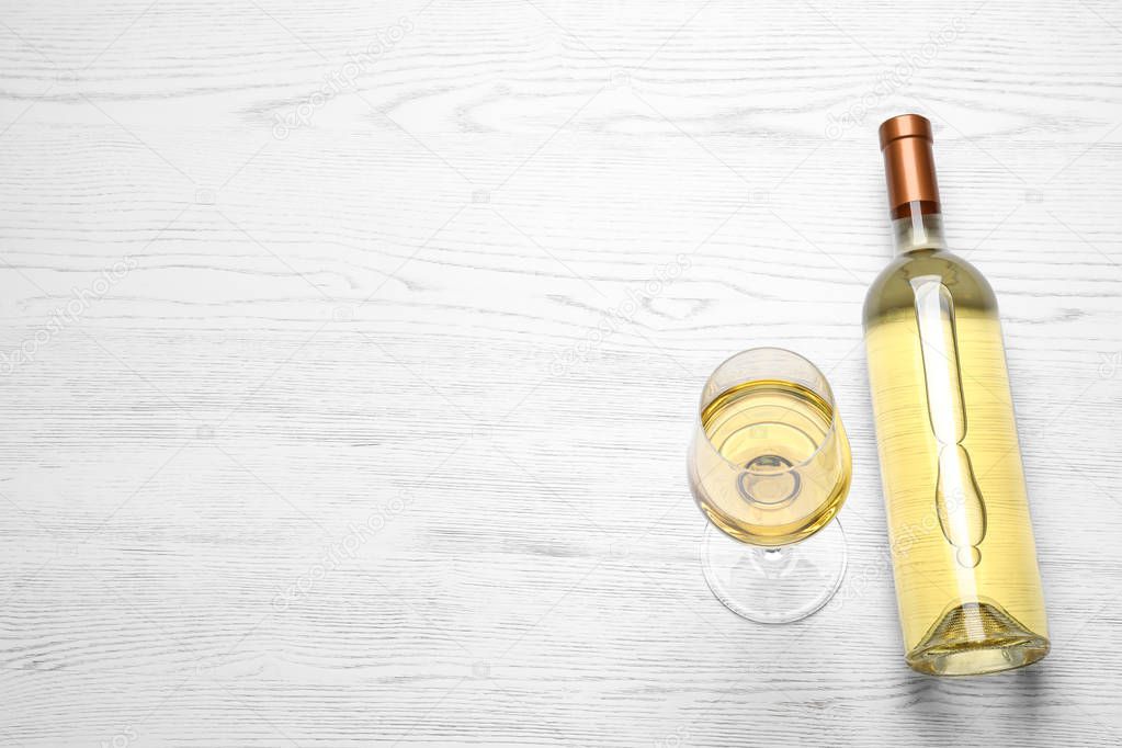 Glass and bottle with white wine on wooden background, view from above. Space for text