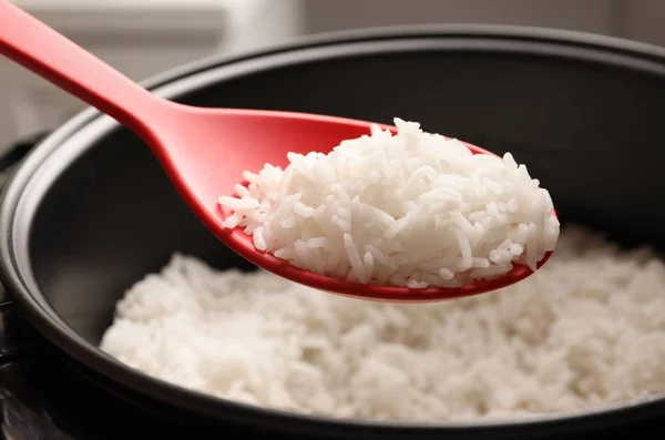 Spoon with tasty hot rice over cooker, closeup — Stock Photo, Image