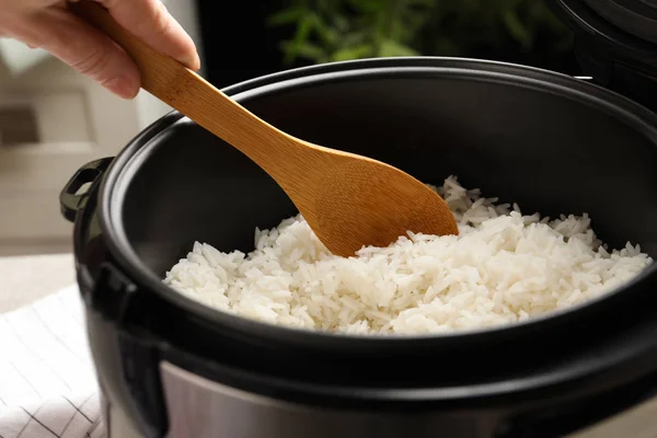 Woman taking tasty rice with spoon from cooker in kitchen, closeup — Stock Photo, Image