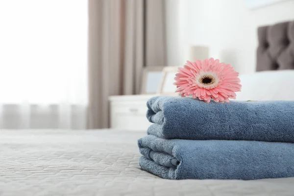 Pilha de toalhas limpas com flor na cama dentro de casa. Espaço para texto — Fotografia de Stock