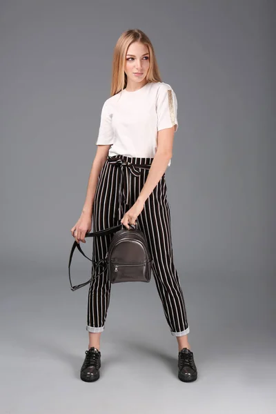 Молода стильна жінка в модному спортивному взутті з рюкзаком на сірому фоні — стокове фото