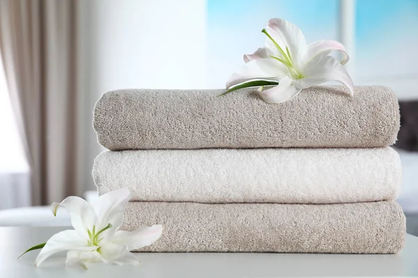 Stack of fresh towels with flowers on table indoors — Stock Photo, Image