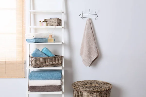 Scaffale e scaffale con asciugamani puliti e articoli da toeletta vicino alla parete bianca — Foto Stock