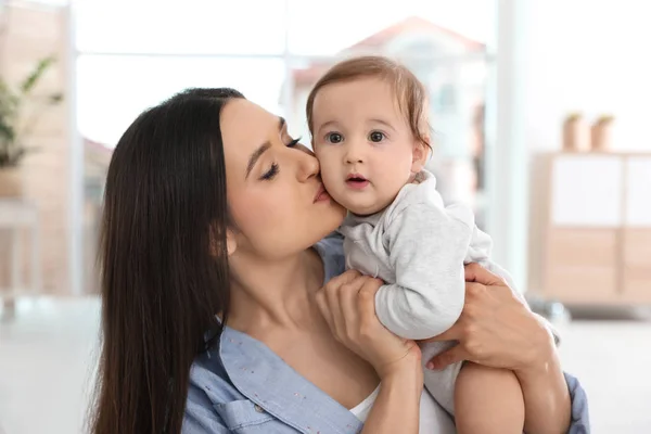 Jovem mãe feliz beijando seu bebê adorável na sala de estar — Fotografia de Stock