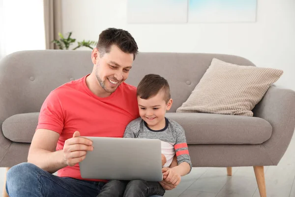 Хлопчик і його батько з ноутбуком сидить біля дивана на підлозі. Сімейного часу — стокове фото