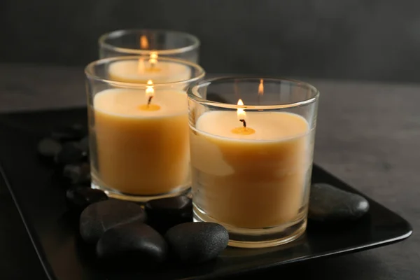 Placa escura com velas acesas e pedras na mesa — Fotografia de Stock