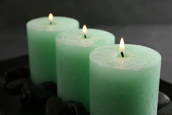 Tres velas ardientes de color y rocas en el plato oscuro —  Fotos de Stock