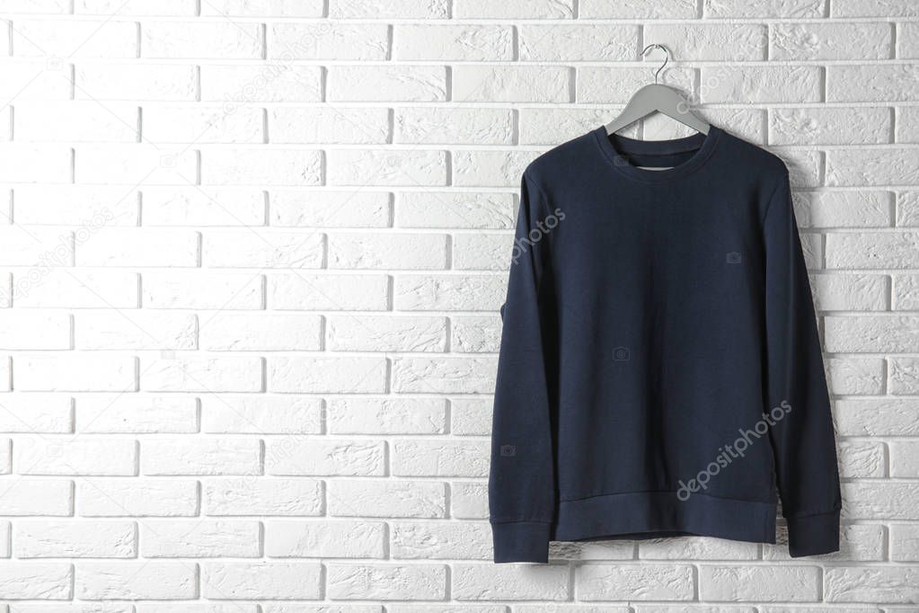 Hanger with dark sweatshirt against brick wall. Mockup for design