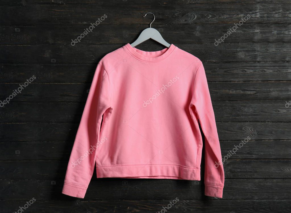 Hanger with pink sweatshirt on wooden background. Mockup for design