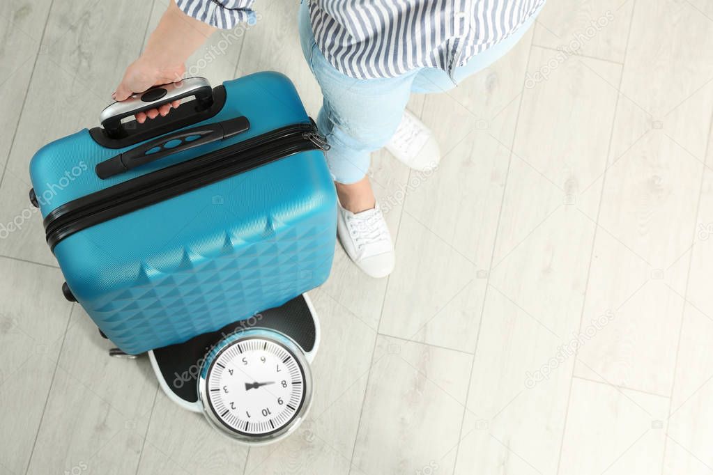 Woman weighing suitcase indoors, top view. Space for text