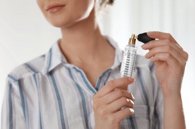 Young woman applying perfume on neck against blurred background, closeup