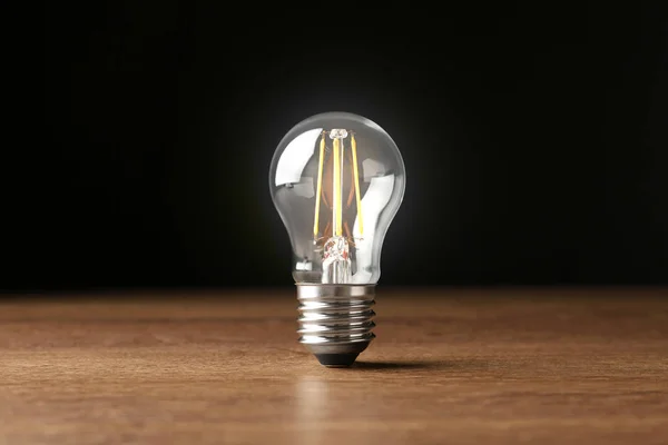 Glowing light bulb for modern lamps on table against black background — Stock Photo, Image