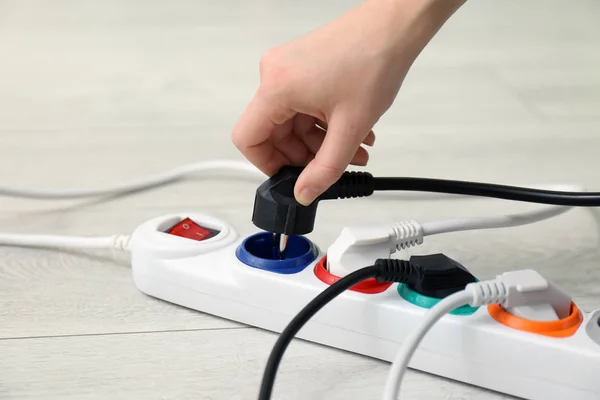 Woman inserting power plug into extension cord on floor, closeup. Electrician\'s professional equipment