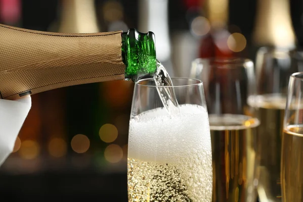 Pouring champagne into glass on blurred background, closeup — Stock Photo, Image