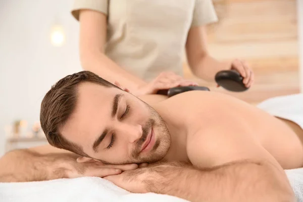 Bonito homem recebendo massagem de pedra quente no salão de spa — Fotografia de Stock