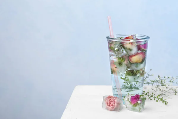Vaso de agua con cubitos de hielo y flores sobre la mesa sobre fondo de color, espacio para texto —  Fotos de Stock