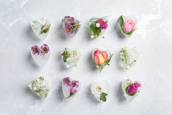 Cubes de glace en forme de coeur avec des fleurs sur fond gris, plat — Photo