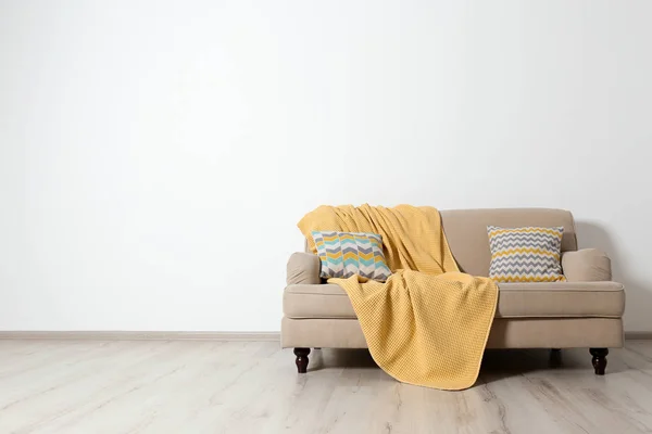 Minimalistisk vardagsrum interiör med soffa, kuddar och pläd nära ljus vägg. Utrymme för text — Stockfoto