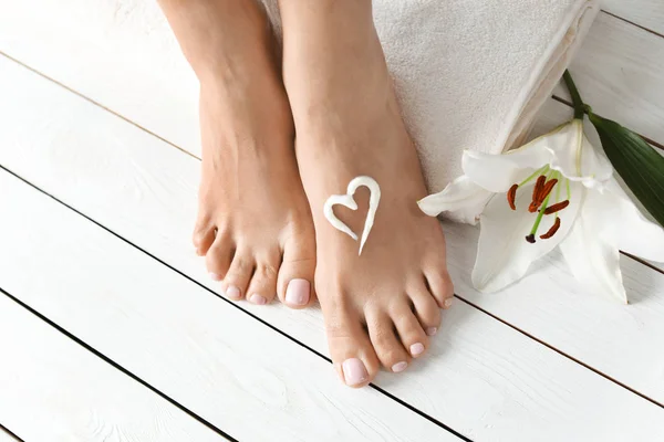 Woman with beautiful feet, cream, flower and towel on white wooden floor, closeup. Spa treatment
