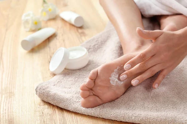 Mujer aplicando crema para los pies sobre la toalla, primer plano. Tratamiento de spa — Foto de Stock