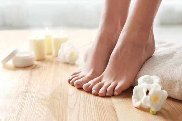 Woman with beautiful feet, towel and flowers on wooden floor, closeup. Spa treatment — 스톡 사진