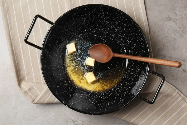 Frying pan with melting butter and spoon on grey table, top view