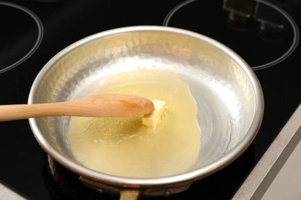 Sartén con mantequilla derretida y cuchara de madera en la estufa, primer plano —  Fotos de Stock
