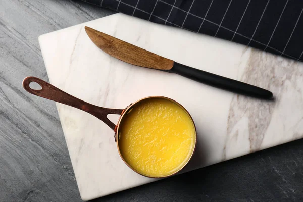 Tablero de piedra con cacerola de mantequilla clarificada y cuchillo sobre mesa, aplanado — Foto de Stock