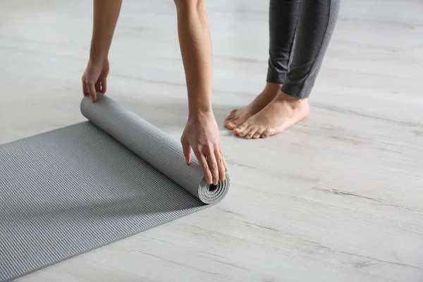 Женщина катает коврик для йоги на полу в помещении, крупным планом — стоковое фото