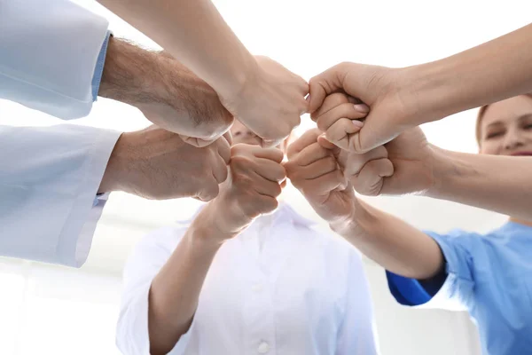 Equipo de médicos poniendo las manos juntas sobre fondo claro, primer plano. Concepto de unidad — Foto de Stock