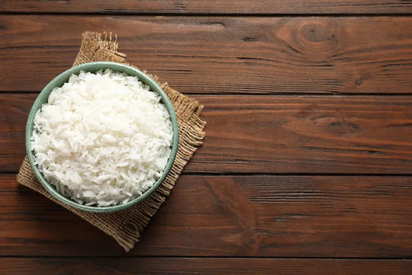 Tigela de arroz cozido saboroso no fundo de madeira, vista superior. Espaço para texto — Fotografia de Stock
