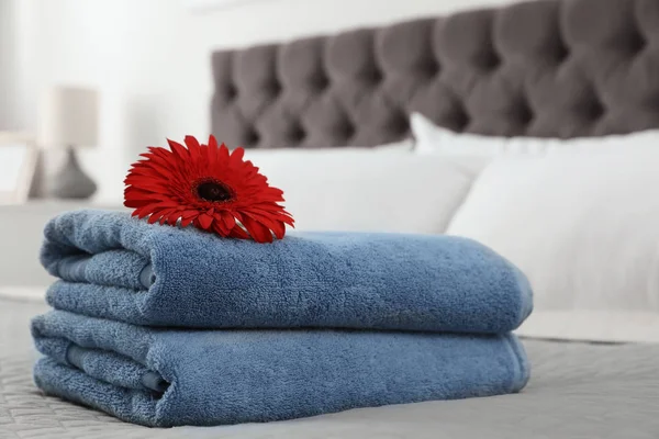 Stack of clean towels with flower on bed indoors — Stock Photo, Image