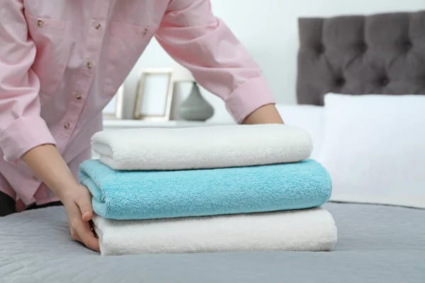 Woman putting stack of clean towels on bed — Stock Photo, Image