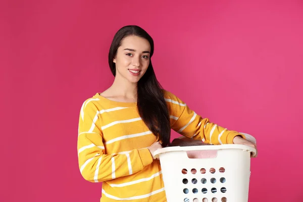 Happy young woman holding basket with laundry on color background — Stock Photo, Image