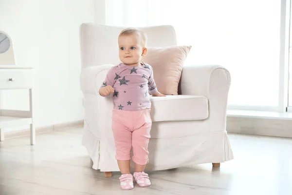 Niedliches kleines Mädchen steht neben Sessel im Zimmer — Stockfoto