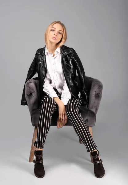 Молода стильна жінка з модним взуттям, що сидить у кріслі на сірому фоні — стокове фото