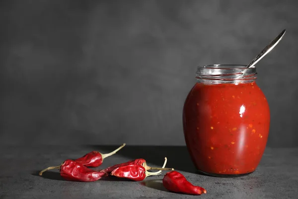 Pot de sauce chili piquante avec cuillère et poivrons sur la table. Espace pour le texte — Photo