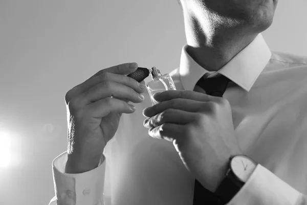 Hombre guapo aplicando perfume en el cuello sobre fondo claro, primer plano. Efecto blanco y negro — Foto de Stock