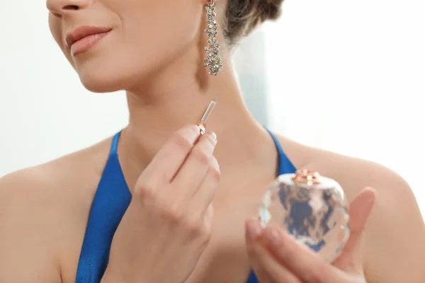 Young woman applying perfume on neck against light background, closeup — Stok fotoğraf