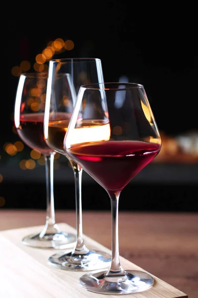 Bicchieri con diversi vini sul tavolo in legno contro le luci sfocate — Foto Stock