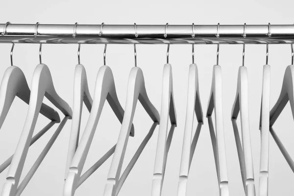 Empty clothes hangers on metal rail against light background, closeup — Stock Photo, Image